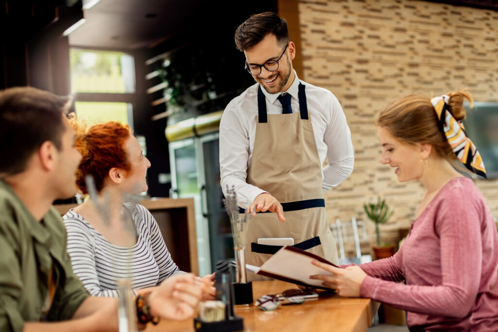 Happy waiter having fun while talking to his guests and taking order from them in a cafe,